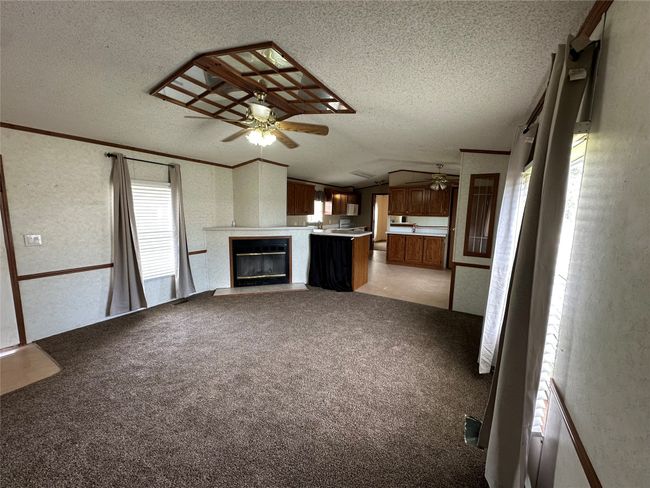 Unfurnished living room featuring ceiling fan, a textured ceiling, lofted ceiling, a glass covered fireplace, and a textured wall | Image 8