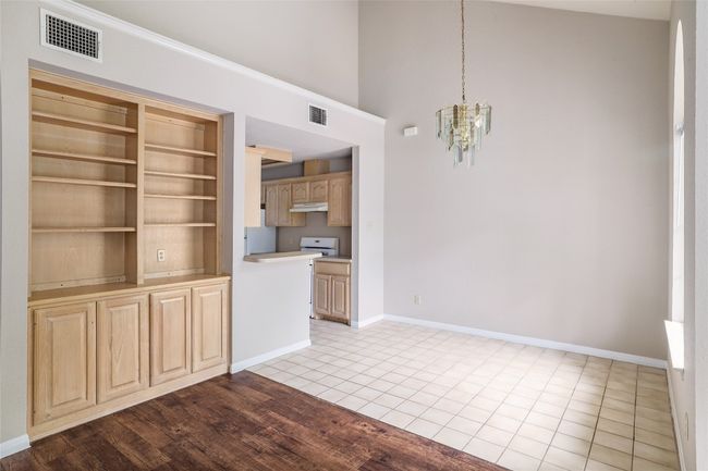 Unfurnished dining area featuring a chandelier, baseboards, a towering ceiling, and tile patterned flooring | Image 8