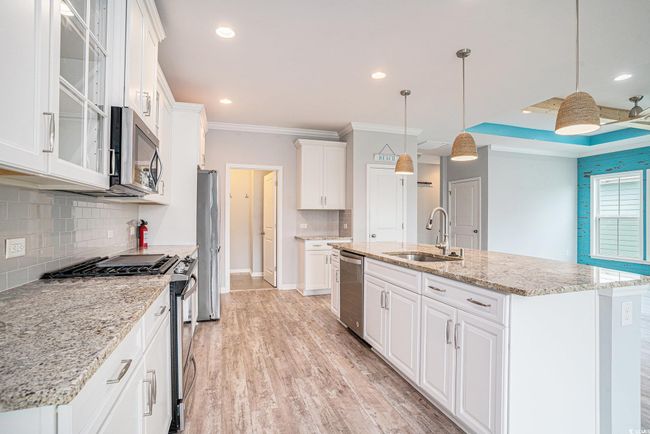 Kitchen with appliances with stainless steel finishes, white cabinets, ornamental molding, backsplash, and light wood-style flooring | Image 9