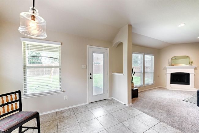 Foyer entrance with light tile patterned floors, a fireplace with raised hearth, lofted ceiling, and light carpet | Image 10