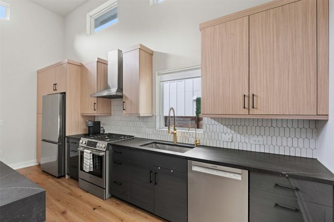 Kitchen featuring appliances with stainless steel finishes, wall chimney exhaust hood, dark countertops, light brown cabinets, and decorative backsplash | Image 6