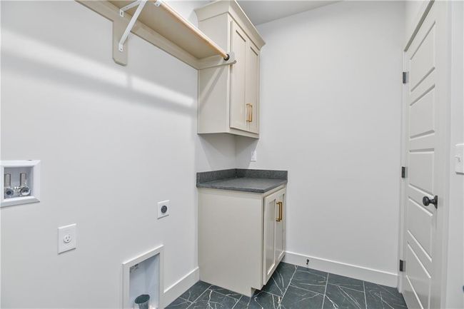 Clothes washing area with dark tile patterned floors, hookup for an electric dryer, and cabinets | Image 30