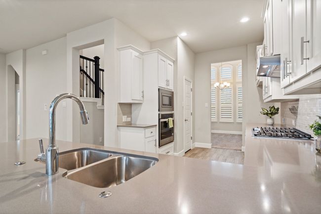 Kitchen featuring appliances with stainless steel finishes, range hood, decorative backsplash, light wood-type flooring, and white cabinets | Image 11