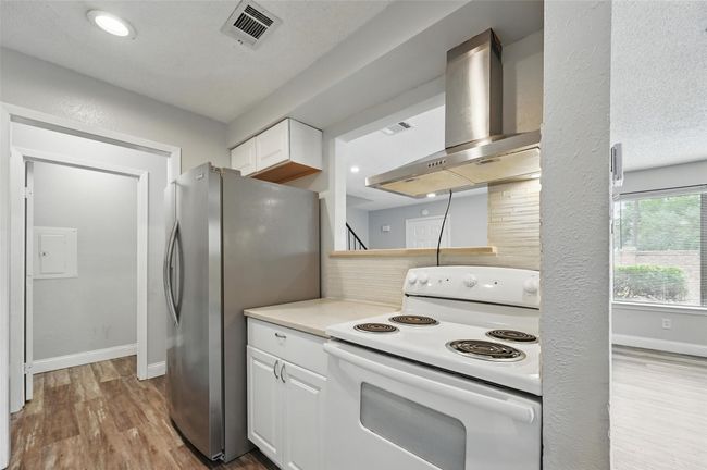Kitchen with white range with electric cooktop, wall chimney exhaust hood, freestanding refrigerator, wood finished floors, and white cabinets | Image 8