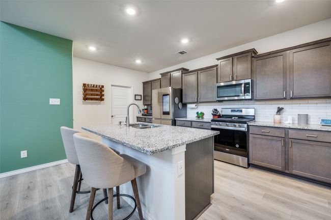 Kitchen featuring dark brown cabinetry, appliances with stainless steel finishes, a center island with sink, a breakfast bar, and light wood-style flooring | Image 4