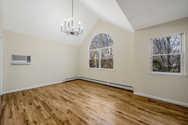 Unfurnished dining area featuring a chandelier, wood-type flooring, baseboard heating, lofted ceiling, and baseboards | Image 18