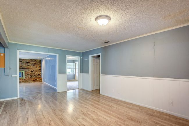 Empty room with wood finished floors, a textured ceiling, ornamental molding, and wainscoting | Image 5