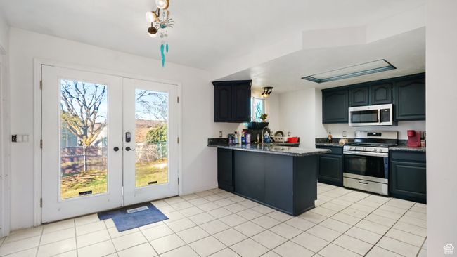 Kitchen featuring a peninsula, stainless steel appliances, dark countertops, french doors, and light tile patterned floors | Image 8