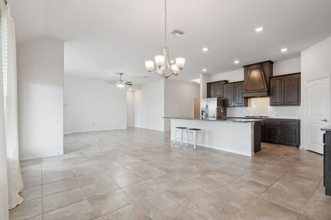 Kitchen featuring premium range hood, a chandelier, stainless steel fridge with ice dispenser, decorative backsplash, and open floor plan | Image 12