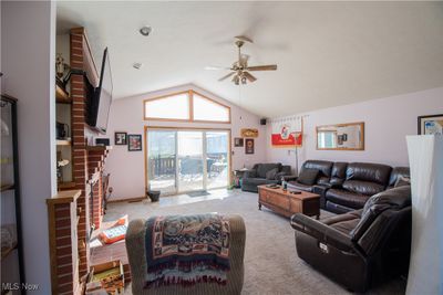 Great room featuring a fireplace, high vaulted ceiling, ceiling fan, and light colored carpet | Image 3