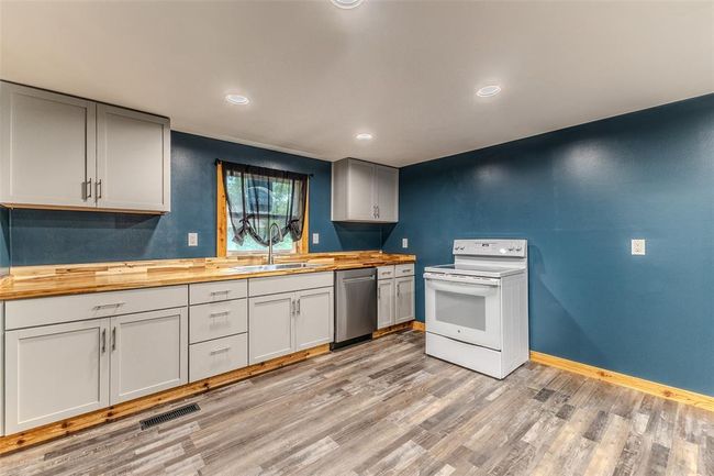 Kitchen featuring electric stove, butcher block counters, stainless steel dishwasher, a sink, and light wood-style flooring | Image 10