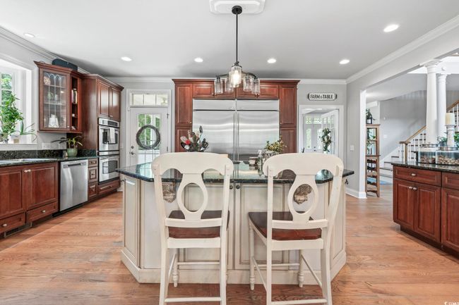 Kitchen featuring appliances with stainless steel finishes, ornamental molding, plenty of natural light, glass insert cabinets, and a kitchen bar | Image 11