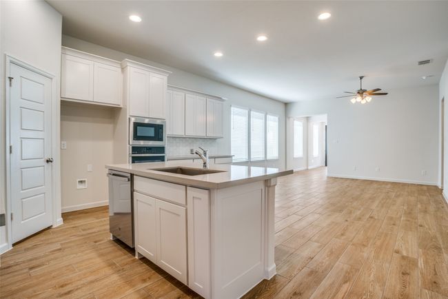 Kitchen featuring stainless steel appliances, a sink, ceiling fan, light wood finished floors, and white cabinets | Image 7