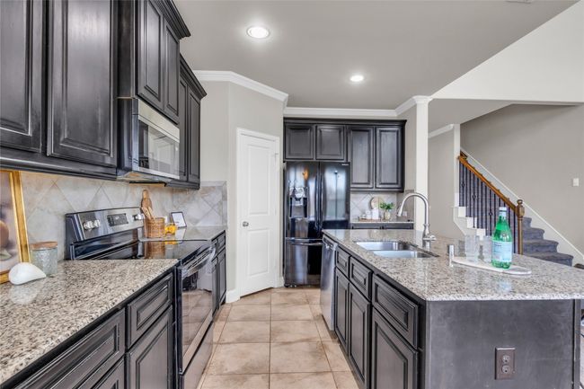 Kitchen featuring appliances with stainless steel finishes, a sink, light stone countertops, a kitchen island with sink, and decorative backsplash | Image 5