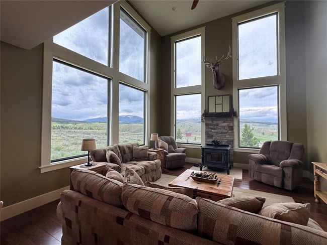 Living area featuring healthy amount of natural light, a wood stove, wood finished floors, and a high ceiling | Image 7