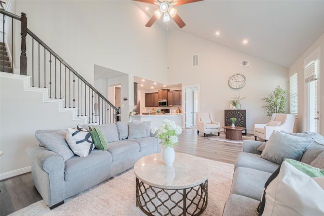 This inviting living room features high ceilings, abundant natural light, and an open layout. A modern kitchen with dark cabinetry is visible in the background, enhancing the home's open concept appeal. | Image 12