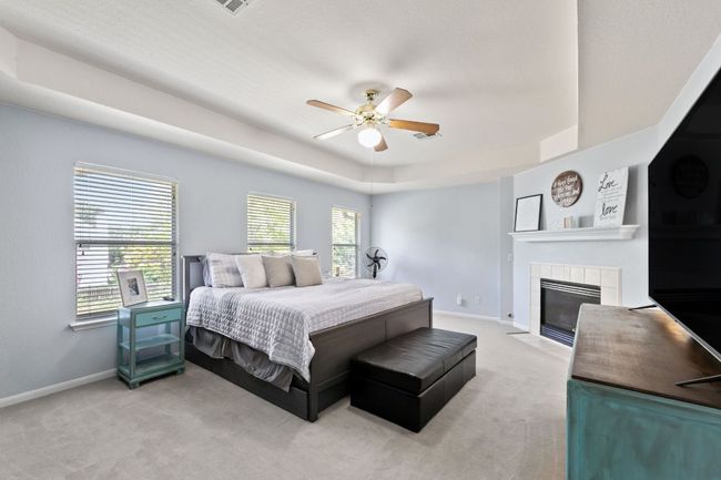 Bedroom with light colored carpet, a tray ceiling, a tile fireplace, and ceiling fan | Image 17