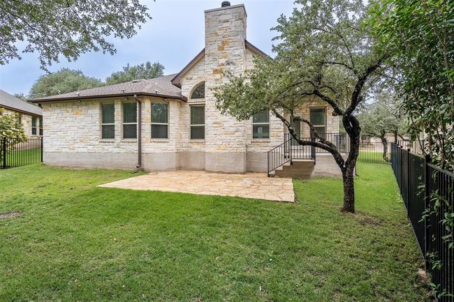 Rear view of property with stone siding, a fenced backyard, a chimney, and a patio area | Image 22