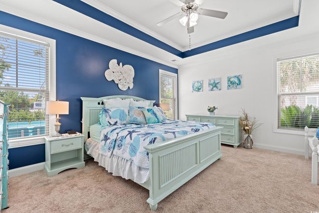 Bedroom with light colored carpet, a raised ceiling, crown molding, and a ceiling fan | Image 17