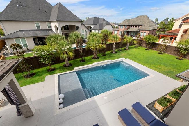 Balcony view of resort-style backyard with sleek modern pool, tanning ledge, and lush landscaping—perfect for relaxing, entertaining, and enjoying year-round outdoor living. | Image 32