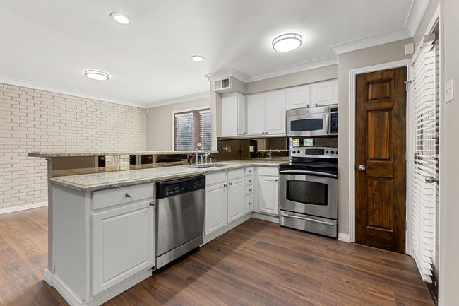 Kitchen featuring crown molding, a peninsula, a sink, stainless steel appliances, and brick wall | Image 7