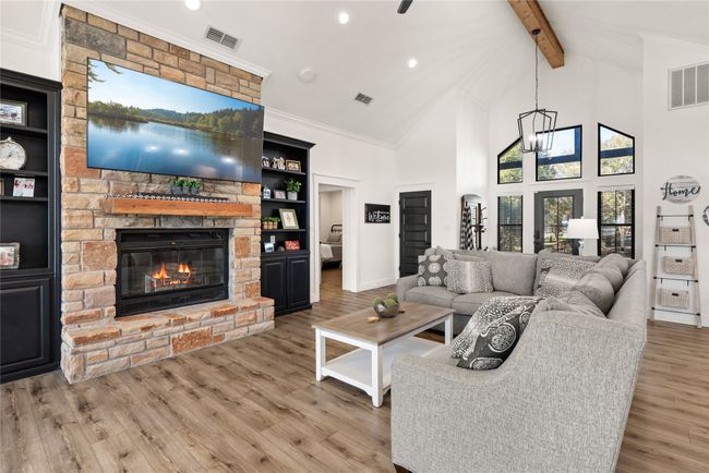 Living room with a stone fireplace, beam ceiling, wood finished floors, high vaulted ceiling, and ornamental molding | Image 14
