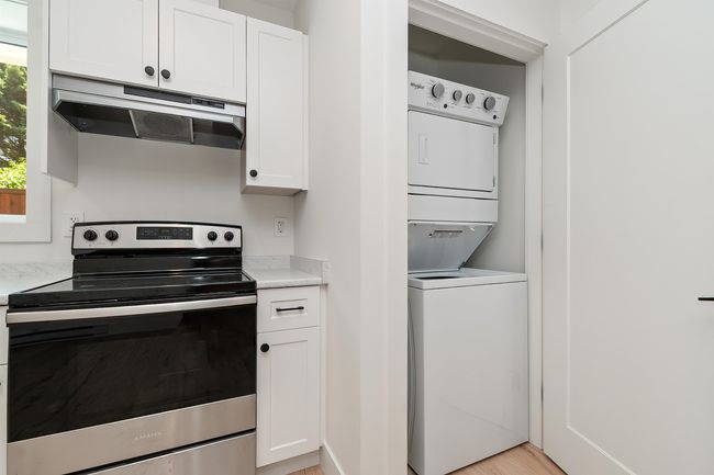 Kitchen with stainless steel electric range oven, estacked washer and dryer, ventilation hood, and light countertops | Image 31