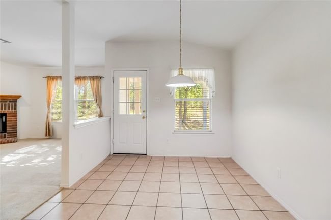 Unfurnished dining area with a brick fireplace, lofted ceiling, light tile patterned floors, and baseboards | Image 17