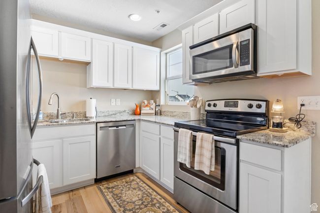 Kitchen featuring visible vents, white cabinets, a sink, stainless steel appliances, and light wood-style flooring | Image 13