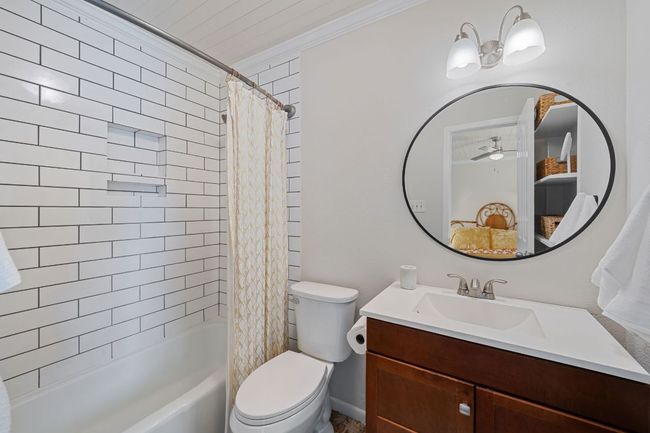 The primary bathroom features updated tile surround, updated vanity, mirror and lighting and also has built-in shelving behind the doorway that perfectly stores your toiletries. | Image 20