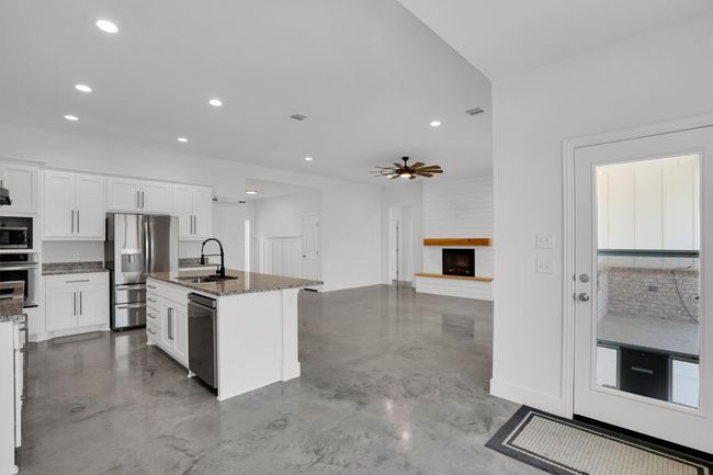 Kitchen with a sink, appliances with stainless steel finishes, finished concrete floors, dark stone counters, and white cabinetry | Image 19