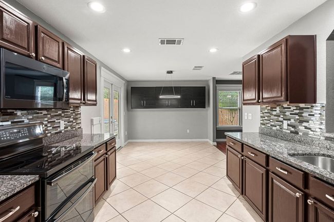 Kitchen featuring range with two ovens, black microwave, backsplash, dark brown cabinetry, and recessed lighting | Image 11