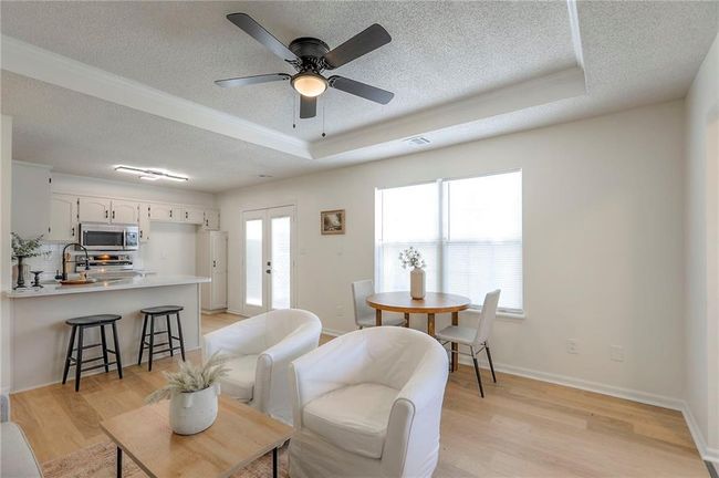 Living room featuring a textured ceiling, light wood finished floors, a raised ceiling, french doors, and a ceiling fan | Image 5
