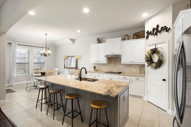 Kitchen with white cabinets, an island with sink, decorative light fixtures, under cabinet range hood, and a sink | Image 17