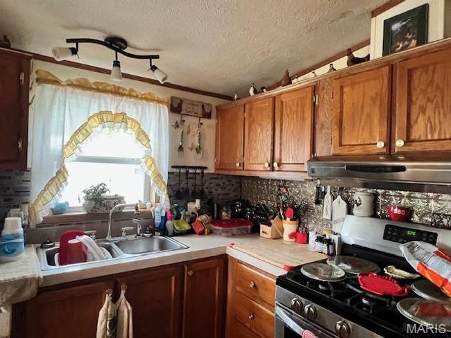 Kitchen with under cabinet range hood, light countertops, brown cabinetry, and a sink. | Image 13