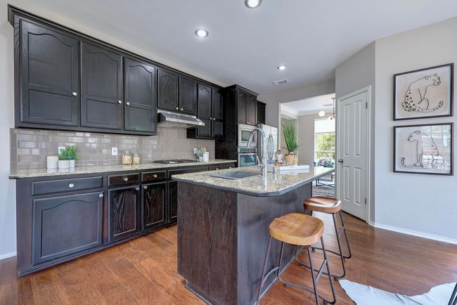 Kitchen featuring baseboards, appliances with stainless steel finishes, wood finished floors, a kitchen bar, and recessed lighting | Image 17