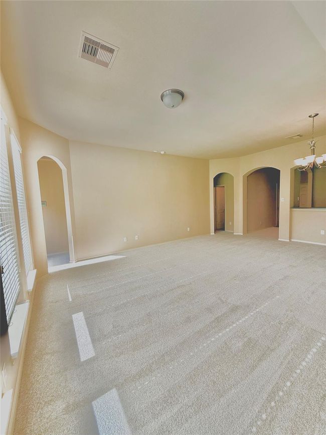 This spacious living area features soft carpet, neutral walls, and ample natural light from large windows. It offers an open layout with arched doorways leading to adjacent rooms, creating a welcoming and versatile space. | Image 21
