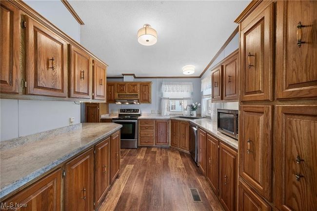 Kitchen featuring stainless steel appliances, ornamental molding, dark wood-type flooring, brown cabinetry, and light stone countertops | Image 8