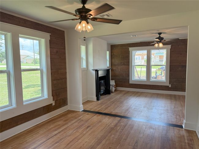 Unfurnished living room featuring wooden walls, wood finished floors, ceiling fan, and plenty of natural light | Image 8
