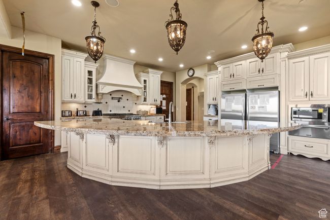 Kitchen featuring dark wood-type flooring, arched walkways, appliances with stainless steel finishes, premium range hood, and backsplash | Image 22