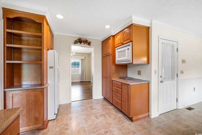 Kitchen with white appliances, brown cabinetry, open shelves, baseboards, and light tile patterned floors | Image 10