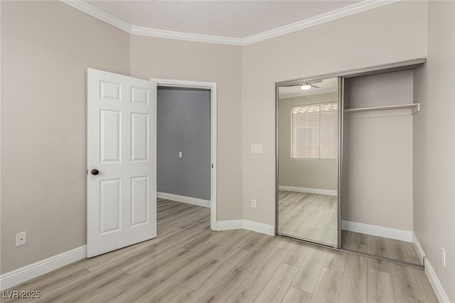 Guest bedroom featuring light wood-style floors, ornamental molding, closet with mirrored doors. | Image 23