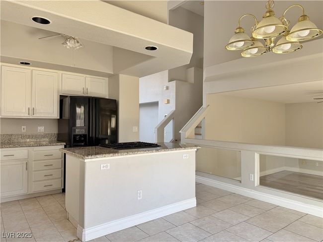 Kitchen featuring gas cooktop, light stone counters, an inviting chandelier, white cabinetry, and black refrigerator with ice dispenser | Image 6