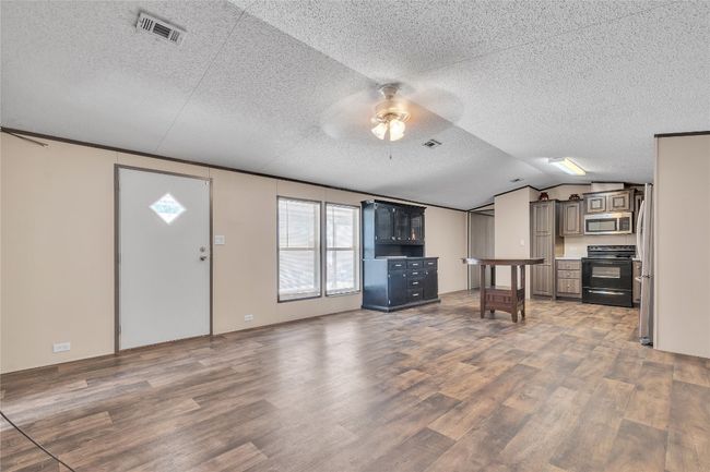 Kitchen with black range with electric stovetop, stainless steel microwave, wood finished floors, a ceiling fan, and a textured ceiling | Image 4