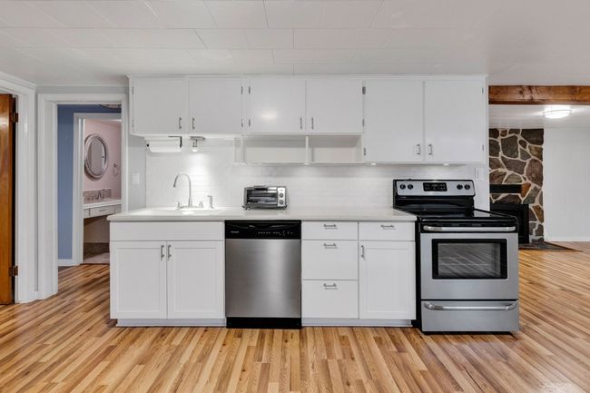 Kitchen with white cabinetry, decorative backsplash, light wood-style flooring, appliances with stainless steel finishes, and light countertops | Image 27