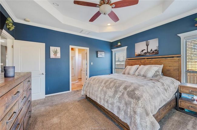 Bedroom featuring a tray ceiling, carpet flooring, crown molding, a ceiling fan, and ensuite bathroom | Image 17
