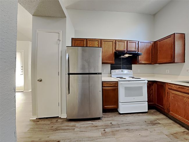 Kitchen featuring freestanding refrigerator, white electric stove, light wood-style floors, under cabinet range hood, and light countertops | Image 5