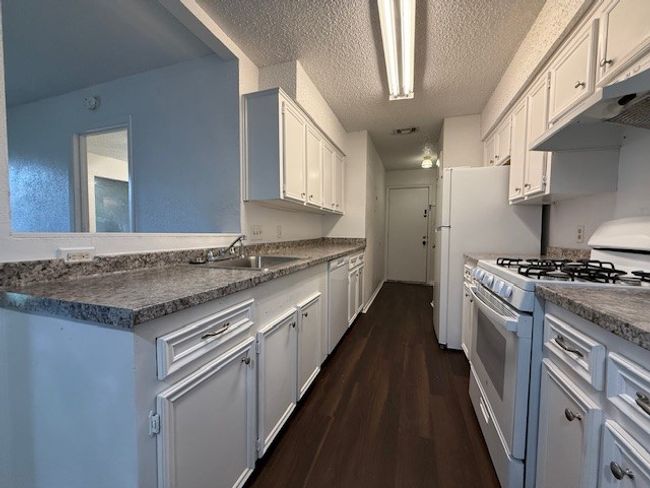 Kitchen with white gas range oven, dishwashing machine, under cabinet range hood, dark wood finished floors, and a textured ceiling | Image 7