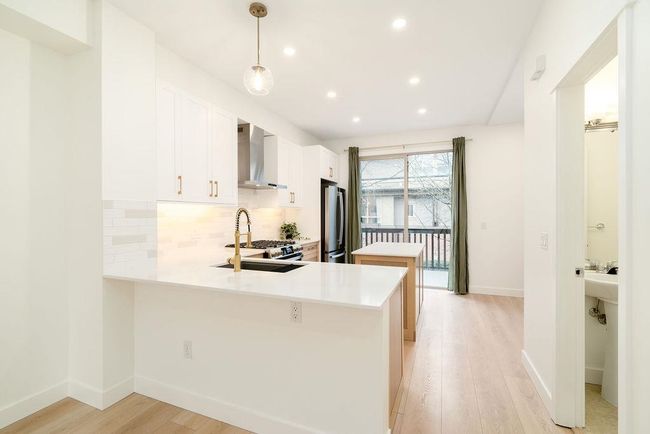 Kitchen featuring tasteful backsplash, a sink, light wood-type flooring, wall chimney range hood, and freestanding refrigerator | Image 9