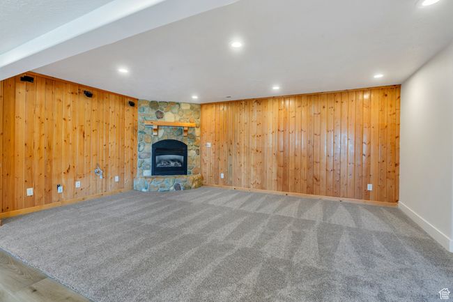 Unfurnished living room featuring wood walls, baseboards, carpet floors, recessed lighting, and a fireplace | Image 19